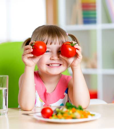 Child with tomatoes. Happy little girl with healthy meal and vegetables at school