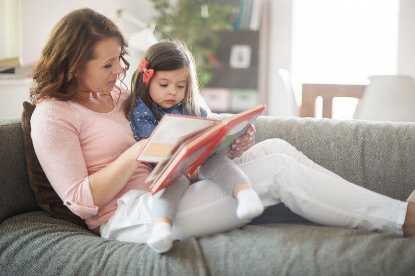 Mom sitting on a couch with her daughter on her lap reading