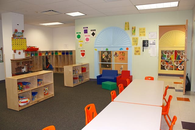A classroom with tables chairs and shelves with toys